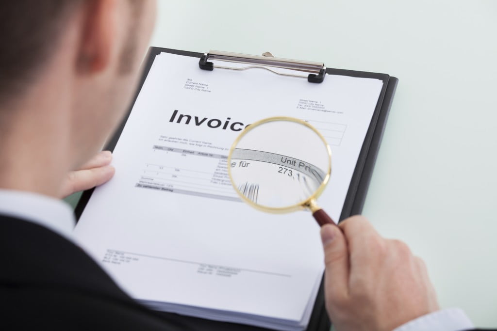 Businessman Examining Invoice Through Magnifying Glass